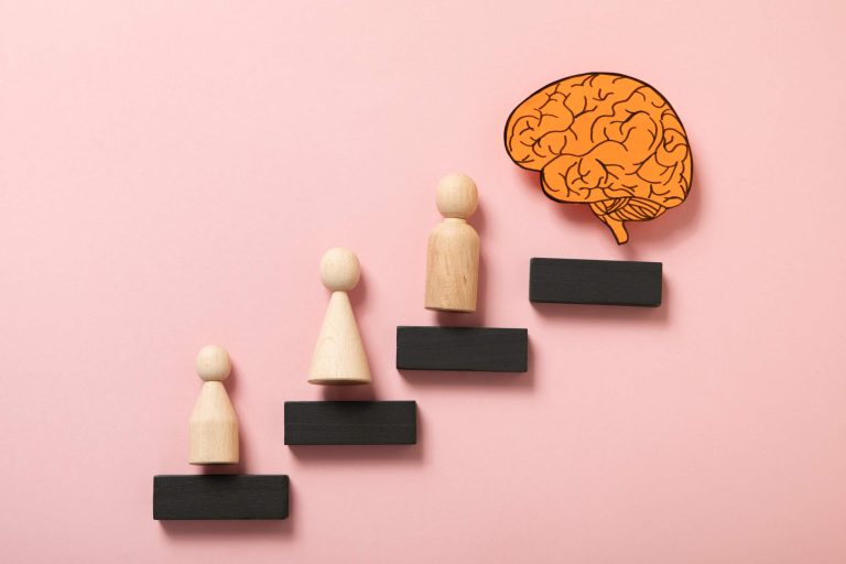 "Wooden figures representing the stages of human growth, moving toward a brain symbol, illustrating learning, emotional development, and personal transformation."