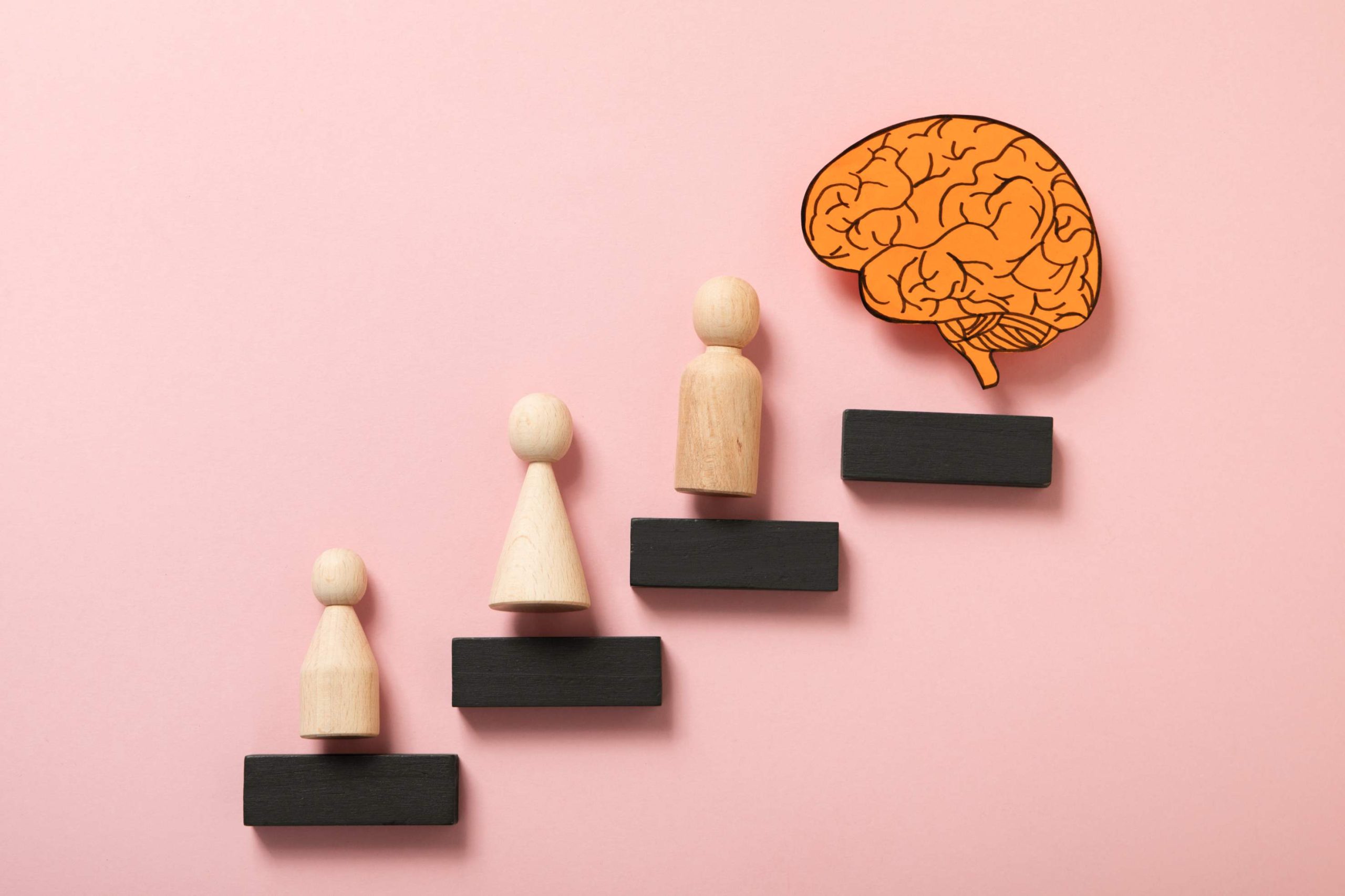 "Wooden figures representing the stages of human growth, moving toward a brain symbol, illustrating learning, emotional development, and personal transformation."